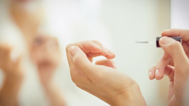 A girl tends to her hands, gently applying cuticle oil along each nail with a small brush. This nail care routine keeps cuticles healthy and nourished, showcasing professional at-home treatment