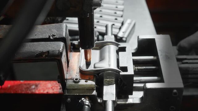 Copper electrode contacting stamped steel automotive bracket inside industrial fixture during spot welding setup, showing precise alignment, metal textures, and machine handling