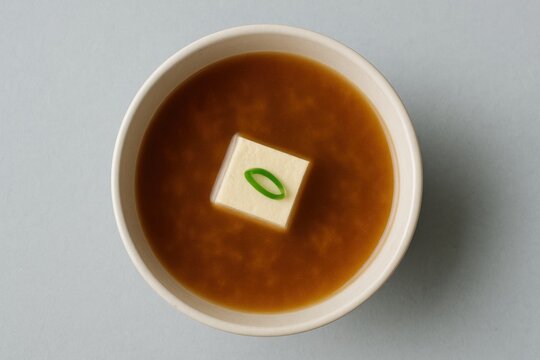 Japanese miso soup in a bowl featuring a square cube of firm tofu topped with fresh green onion slice