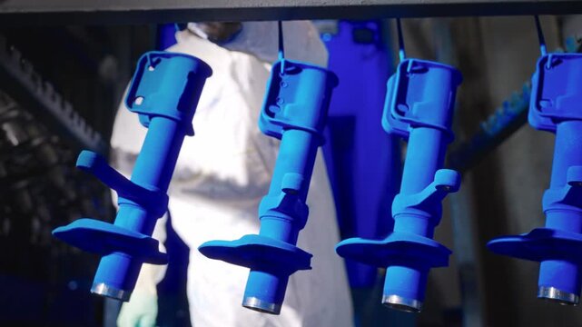Suspended automotive parts after powder coating on overhead conveyor with blurred technician at coating booth