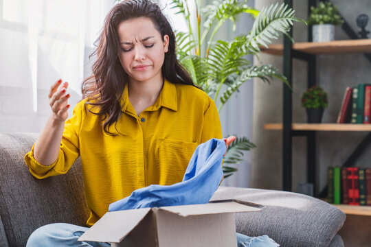 Unhappy young mixed race woman holding cardboard box, dissatisfied customer disappointed with wrong item delivery, online shopping problem and e-commerce concept