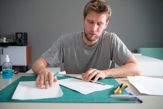 A male student works on engineering designs, using tools and papers on a table in a study area