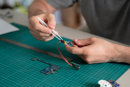 A person uses a tool to connect wires on a circuit board while sitting at a table in a workspace during the day