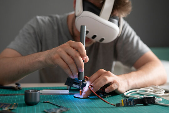 A VR engineer focuses on a virtual reality project while using tools and a headset in a well-lit workspace