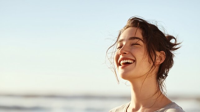 Joyful young woman embracing the ocean breeze with a serene smile while basking in the warm sunlight