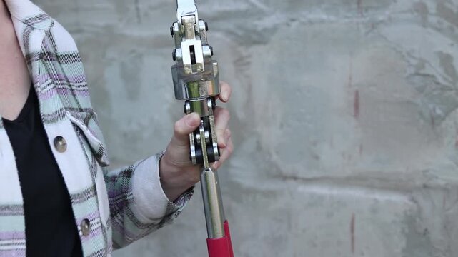 Professional hydraulic press pliers for metal-plastic pipes in female hands. Hydraulic manual press for pressing fittings on PEX pipes. DIY repair concept. Specialized hydraulic equipment