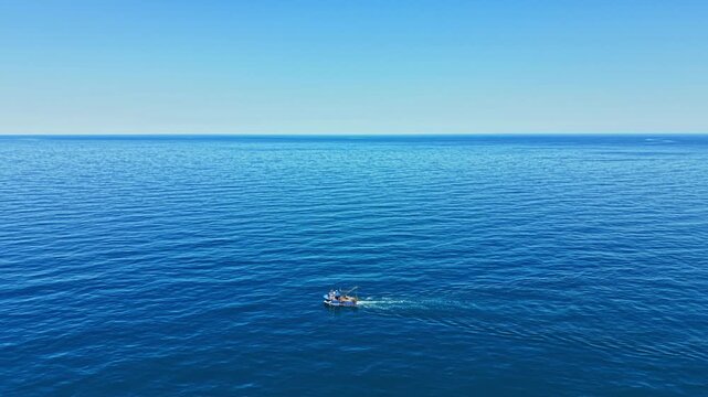 A small boat travels across the blue ocean water under a clear sky during midday. The scene shows wide water with gentle waves. It captures the simple joy of being on the water.
