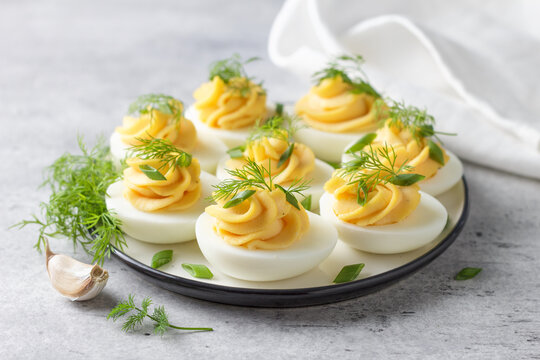 Boiled eggs stuffed with garlic and mayonnaise filling, garnished with fresh dill and green onion. Protein rich appetizer served on a plate, close up view