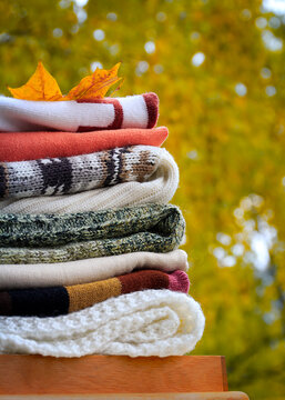 Stack of folded knit sweaters with autumn leaf - cozy seasonal fashion and home comfort