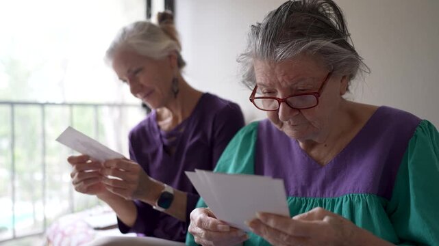 Mature daughter spends time with her elderly mother at a senior care facility looking at old photos and sharing stories from the past