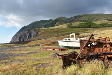 Naklejka premium Abandoned rusty bulldozer and old boat on a grassy slope of a coastal landscape with dramatic cliffs with a dramatic cloudy sky, Corvo Island, Azores