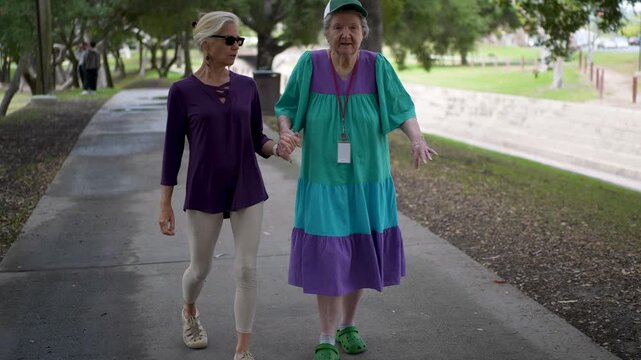 Daughter spends quality time with her mother walking through a park, talking and sharing memories while being happy together.