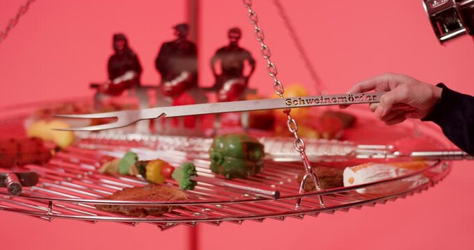 Hand using long metal tongs to move food on a hanging circular barbecue grill