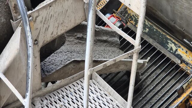 High angle diagonal shot from behind a concrete mixer truck pouring wet concrete into a pump hopper