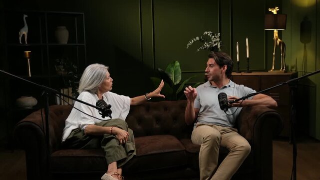 Two people sitting on a sofa and talking into microphones during a broadcast in a studio