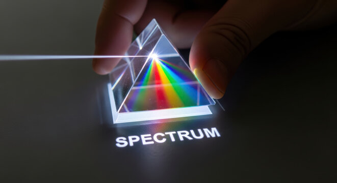 Light spectrum prism with rainbow colors dispersing through glass held by hand showing nuclear fusion research concept