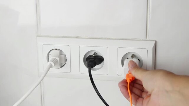 Close-up of a female hand plugging an electrical power plug into a wall socket. Everyday household action showing connecting an electronic device to the power supply, home electricity.
