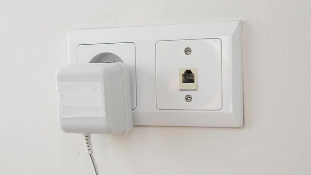 Close-up of a female hand plugging an electrical power plug into a wall socket. Everyday household action showing connecting an electronic device to the power supply, home electricity.