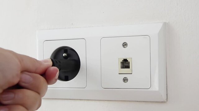 Close-up of a female hand plugging an electrical power plug into a wall socket. Everyday household action showing connecting an electronic device to the power supply, home electricity.