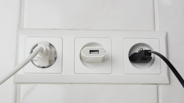 Close-up of a female hand unplugging one USB cable from a wall power adapter and connecting another cable. Everyday technology concept showing charging accessories, USB connection.
