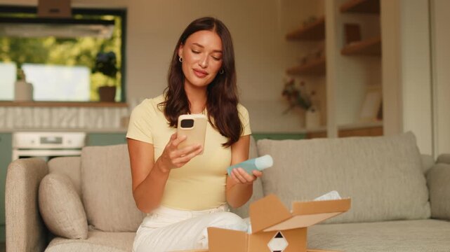 Woman checking beauty product after unboxing delivery at home and using smartphone