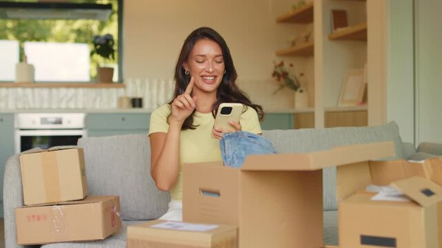 Cheerful young shopaholic woman checking smartphone surrounded by several parcel boxes
