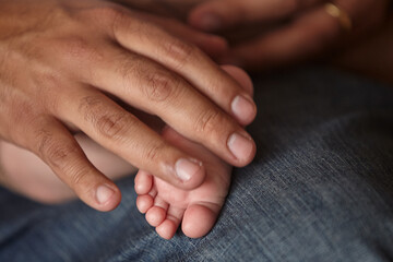 Fototapeta premium A father's strong hands cradles the tiny, perfect foot of his newborn daughter with extraordinary tenderness. The contrast tells the whole story without a single word: large, weathered and capable on 