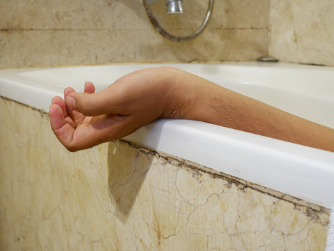 ​Dead man hand hanging out of bathtub close up, crime scene concept of suicide or murder in a bathroom, lifeless human body in a tub