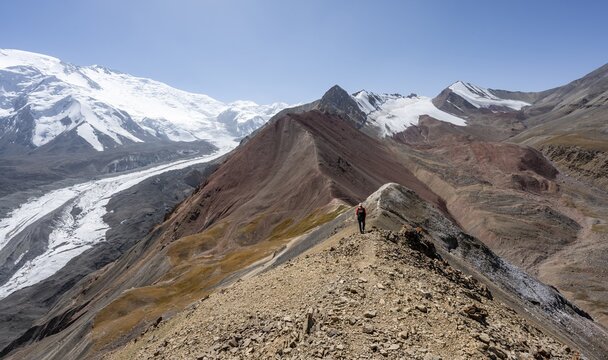 Mountaineer at Traveller's Pass with view of impressive mountain landscape, high mountain landscape with glacier moraines and glacier tongues, glaciated and snow-covered mountain peaks, Lenin Peak and Peak of the XIX Party Congress of the CPSU, Trans Alay Mountains, Pamir Mountains, Osh Province, Kyrgyzstan