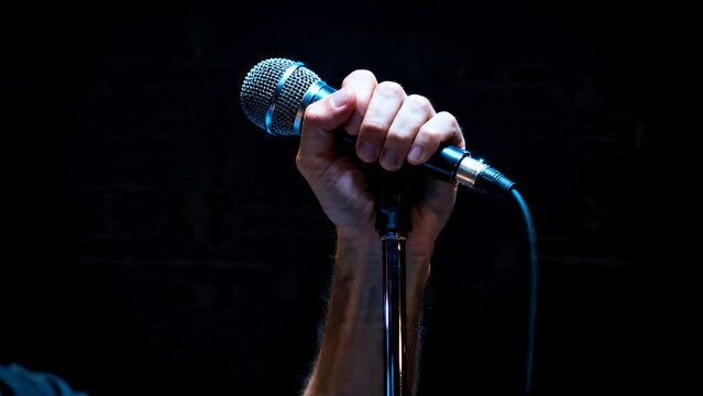 Close-up of hand holding dynamic microphone on black background