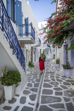 Young woman with dress walking through alley with Cycladic houses, old town of Parikia, Paros, Cyclades, Greece