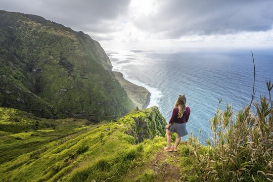 Young woman enjoying view of cliffs and sea, coastal landscape, viewpoint Ponta da Leideira, near Calhau das Achadas, Madeira, Portugal