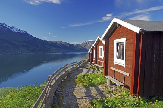 Red wooden cabins on a campsite, view of the fjord and mountains, Hardangerfjord, Fylke Vestland, Norway