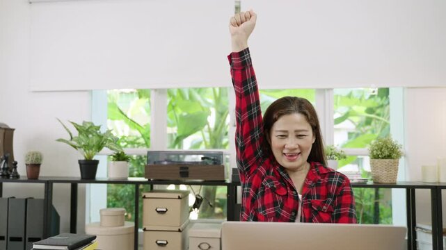 Yeah! Happy excited Asian businesswoman sitting using a laptop computer to check email and message, receiving good news about business work and a big seal deal closed with joy at desk in the office. 