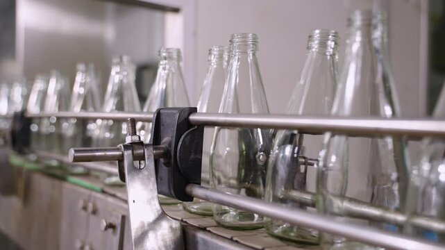 Empty glass beverage bottles on an automatic conveyor belt in a manufacturing plant. Technology for manufacturing bottles and filling fruit juice. Drinking water bottle on factory production conveyor.