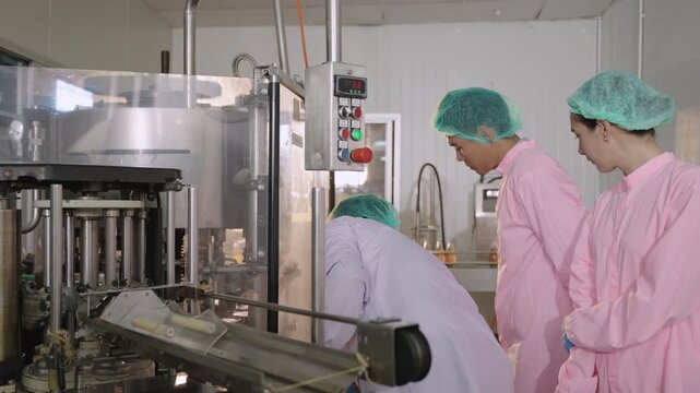 Asian senior technician engineer inspector and machine operator in uniform of food and drink factory explaining and discussing operation of machinery used in beverage production in a manufacturing. 