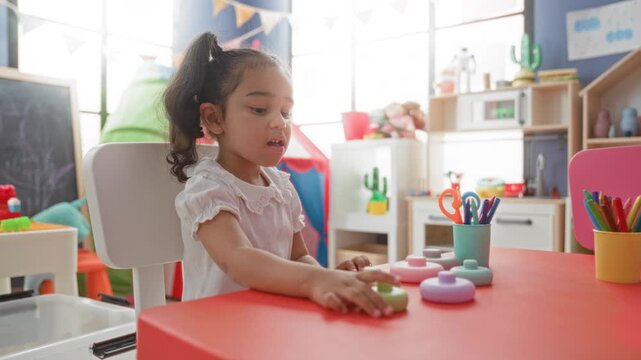 Girl stacking pastel toy rings with hands at a play table inside building; concentration learning focus.
