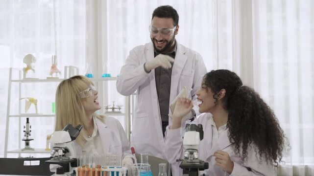 Happy and smiling diverse group of scientists wearing lab coats making high-five gesture after success in experiments and research for a medicine vaccine development together in science laboratory. 