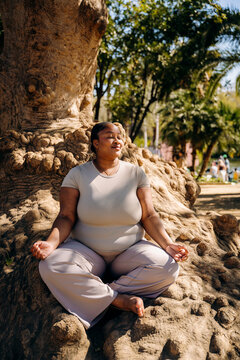 A woman meditates sitting on the root of a tree