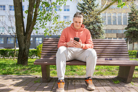 Young guy looking at a phone sitting on a bench in the park