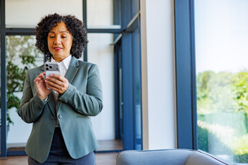 Fototapeta premium Professional mature businesswoman using a smartphone, connecting and communicating in a modern office environment