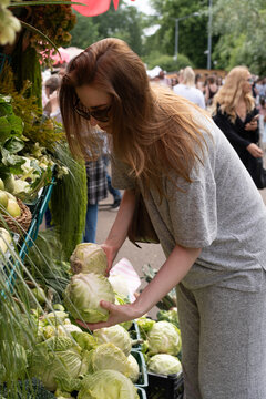 A woman selects fresh cabbage at an outdoor farmers market