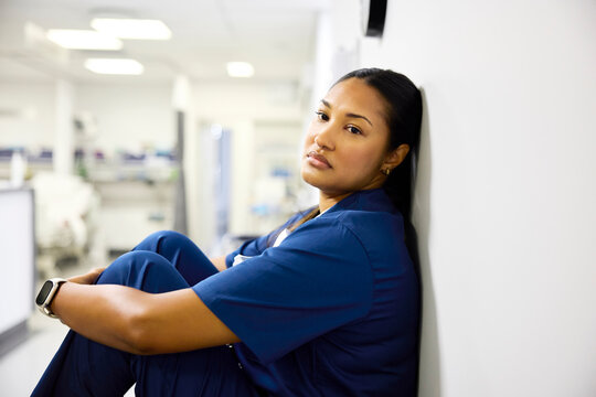Nurse Sits Against Wall in Hospital Hallway