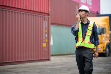 Fototapeta premium Warehouse worker using walkie talkie to communicate during the work shift in the cargo containers area
