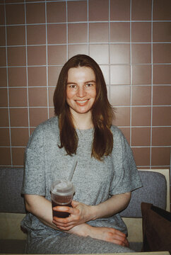 A woman holds a cold drink against pastel tile in a caf&eacute;