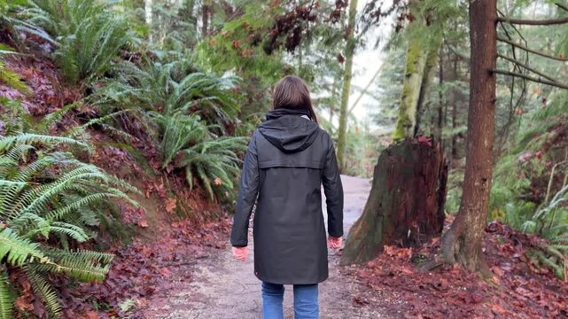 Woman walking on forest trail in Vancouver rainforest, back view with rain jacket