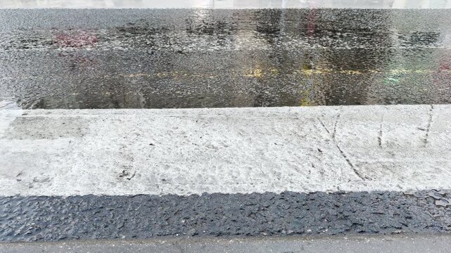 A layer of slick rainwater covers a wide white zebra crosswalk after a storm. The glossy asphalt surface brings a quiet, contemplative, and lonely atmosphere to the empty urban street.