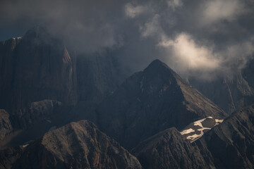 Fototapeta premium Dramatic and atmospheric mountain landscape featuring jagged peaks under heavy, moody clouds. Perfect for travel, nature, and adventure-themed backgrounds.