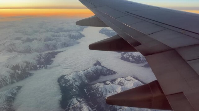 Airplane wing over snow capped mountains and glacier near Banff, aerial sunset view