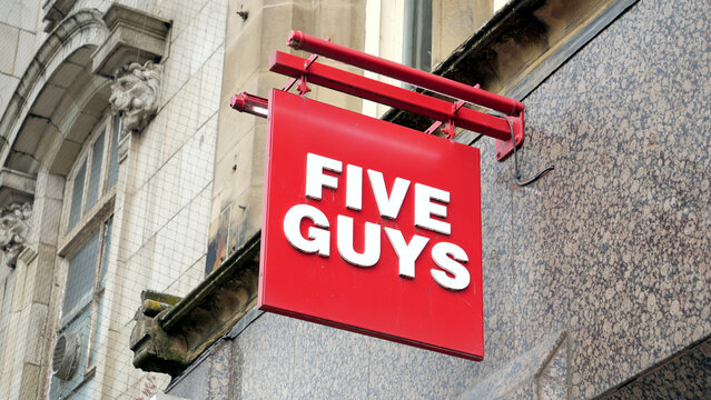 Manchester, England, UK - 18 June 2026: Five Guys sign, American burger restaurant logo close up, red outdoor banner hanging on historic building stone facade